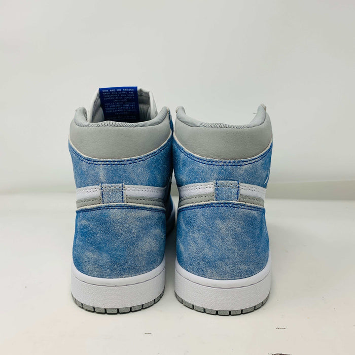 The Jordan 1 Hyper Royal, a high-top sneaker in white and light blue with a gray Nike swoosh and iconic Air Jordan logo, is showcased on a black and red Nike shoebox. It includes extra laces and features a crisp white midsole.