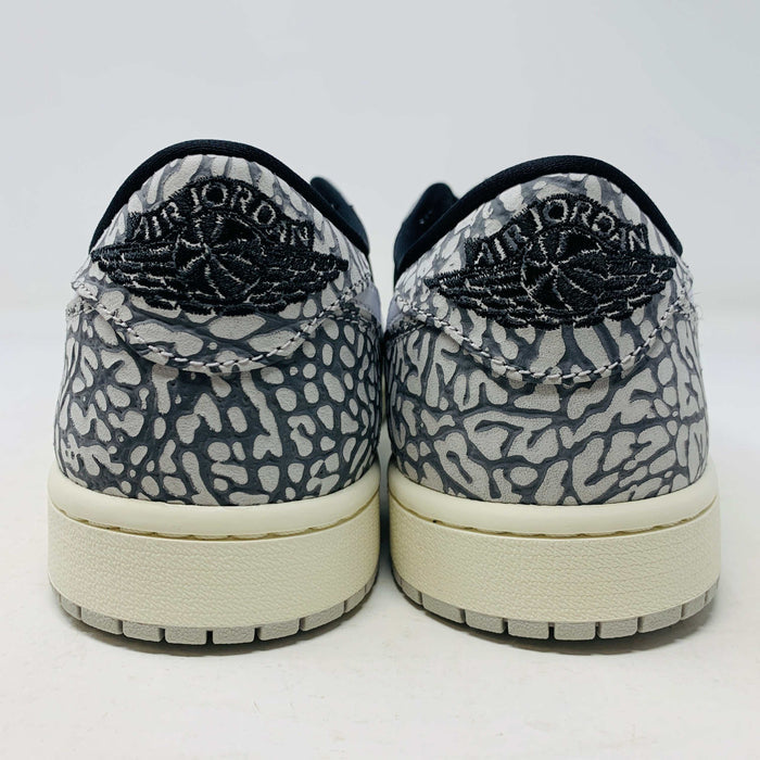 The Jordan 1 Retro Low OG Black Cement sneaker, with black and gray elephant print and a white swoosh, is showcased on a matching shoe box. A small brown box with extra laces is beside it, all set against a plain background.