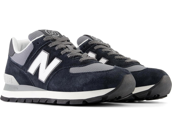 New Balance 574 Rugged sneakers in navy blue suede and gray ripstop material with white branding and durable outsole, angled front view.
