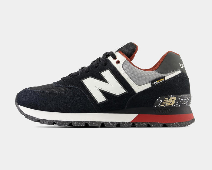 New Balance 574 Rugged sneakers in black with white "N" logo, suede and mesh upper, red accents, and speckled midsole, side view.