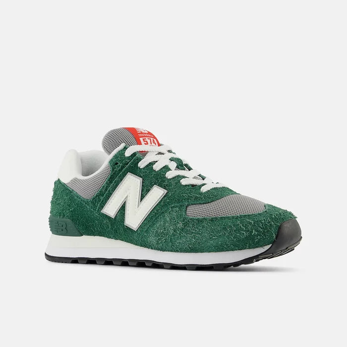 New Balance 574 sneakers with green textured suede upper, gray mesh details, white leather logo overlay, and red branding, angled front view.