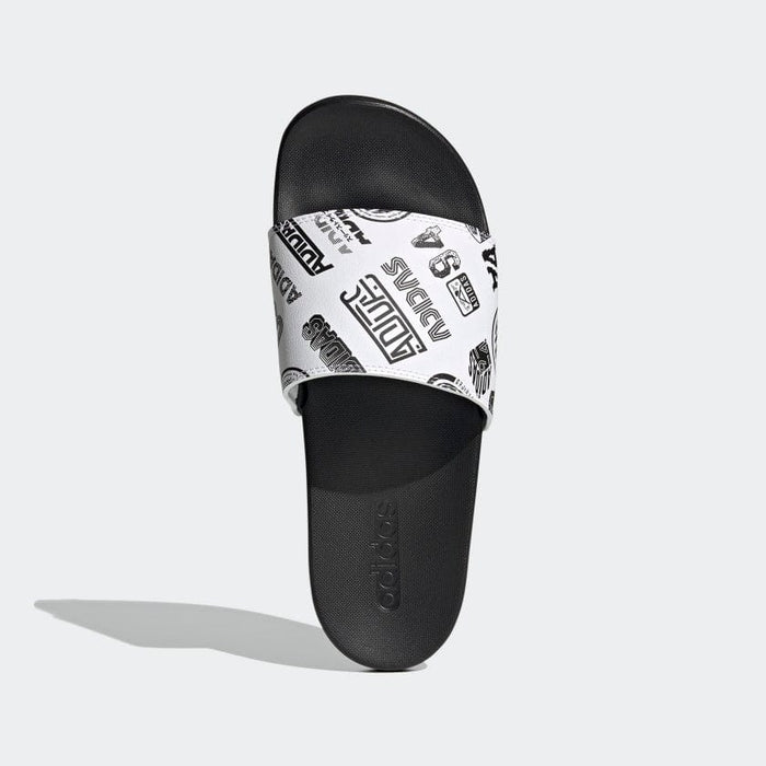 Adidas Adilette Comfort Slides in black with a white patterned strap featuring logo graphics, top view.