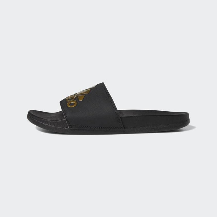 Adidas Adilette Comfort Slides in black with gold logo detailing, side view showcasing contoured footbed and slip-on design.