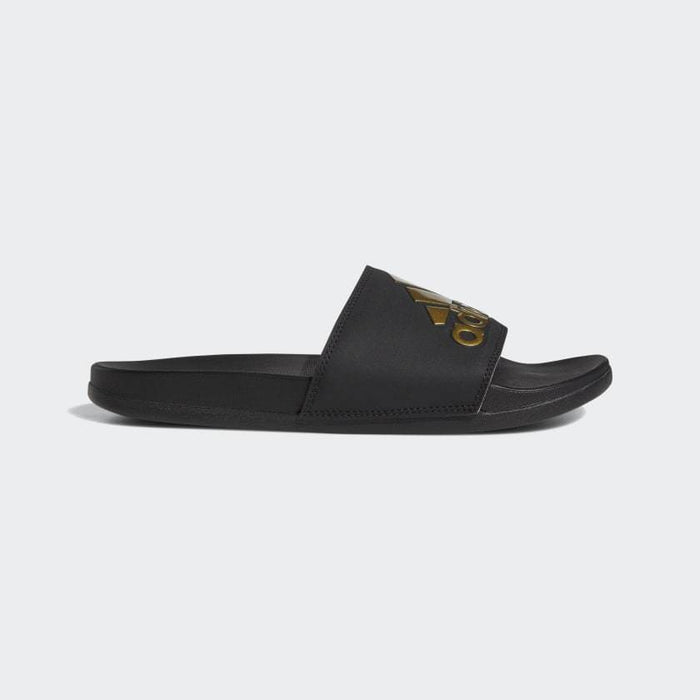 Adidas Adilette Comfort Slides in black with gold logo detailing, side view showing contoured footbed and slip-on design.