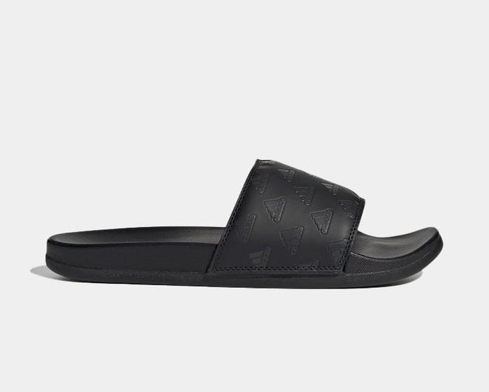 Adidas Adilette Comfort slides in black with embossed Adidas logo patterns and cushioned footbed, side view.