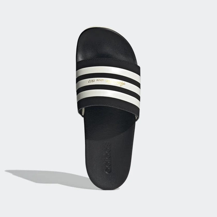 Adidas Adilette Comfort slides in black with white stripes and gold text detail, top view showing soft footbed and textured sole