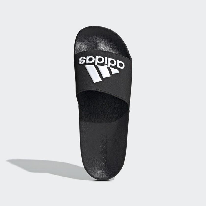 Adidas Adilette Shower Slides in black with embossed Adidas logo in white on the strap, top view showing contoured footbed design.