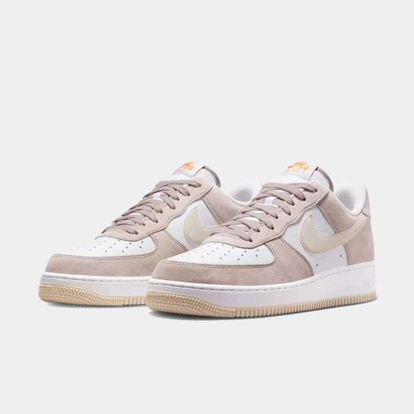 Nike Air Force 1 '07 sneakers in white and light taupe with suede overlays, perforated toe box, and orange branding, front angle view.
