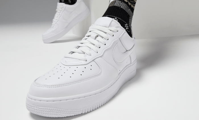 Nike Air Force 1 '07 sneakers in white leather with perforated toe box and signature Swoosh logo, angled front view worn casually.