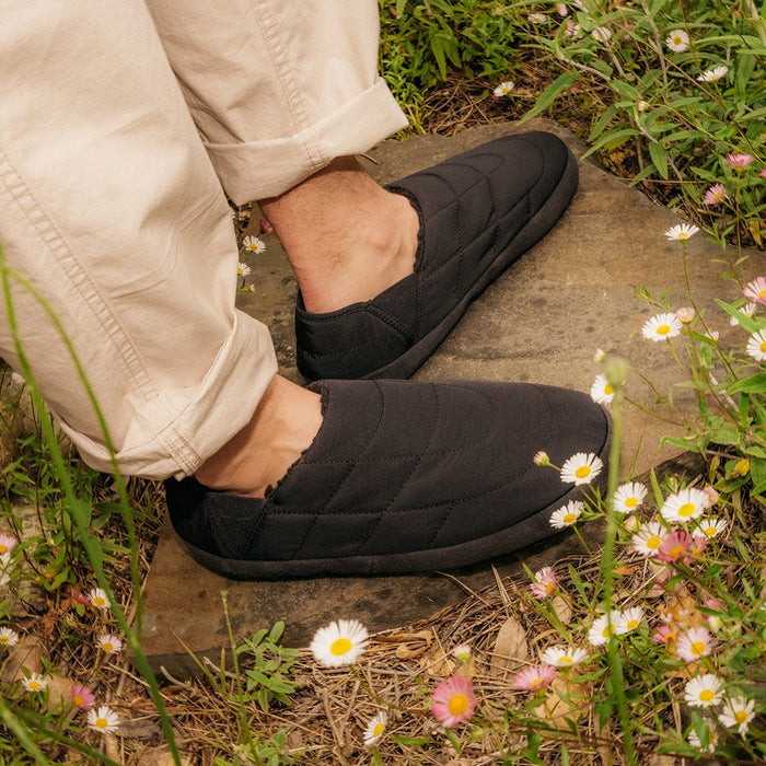 SeaVees Apres Puff Slip On shoes in black with quilted puff design, worn outdoors among flowers.