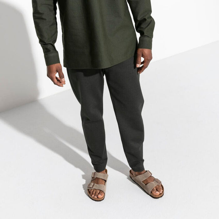 Birkenstock Arizona Suede sandals in taupe with adjustable two-strap buckles and cork footbed, worn by a person standing.