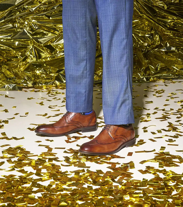 Stacy Adams Bennett Wingtip Oxford shoes in cognac brown leather with brogue detailing and lace-up closure, worn in a festive setting.