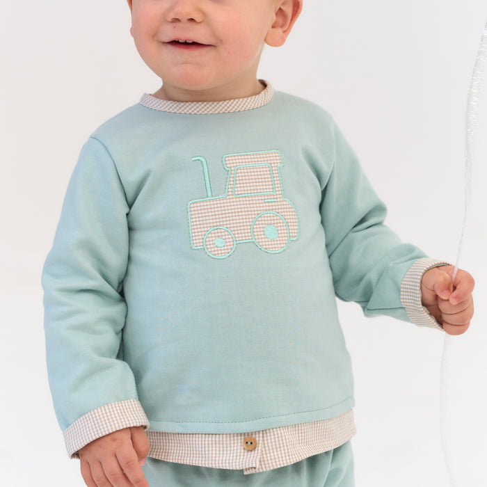 Child wearing a light blue sweatshirt with a tractor design on a plain background