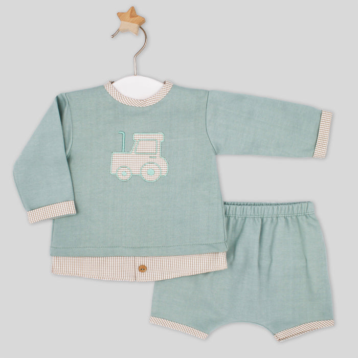 Children's outfit with a green shirt and shorts featuring a truck design on a light gray background.