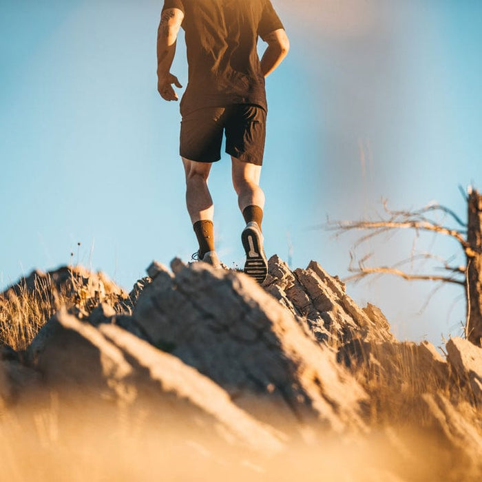 Darn Tough Boot Midweight Tactical Sock with Cushion in olive green worn by hiker on rocky terrain.