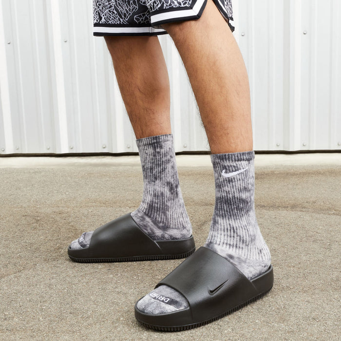 Nike Calm Slide sandals in black with a sleek design and contoured footbed, worn outdoors.