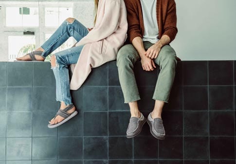 Sanuk Chiba slip-on shoes in gray with textured canvas upper and casual loafer design, lifestyle context worn by sitting individuals.