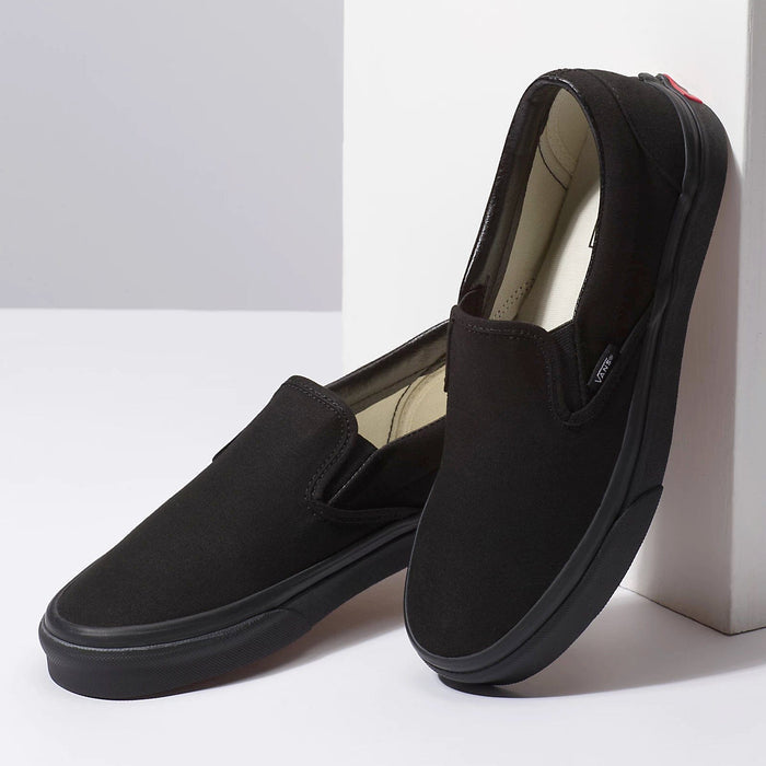 Vans Classic Slip-On shoes in solid black canvas with elastic side accents and black rubber outsole, angled side view.