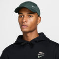 Nike Club Hat in dark green with embroidered white logo, front view worn above a black hoodie.