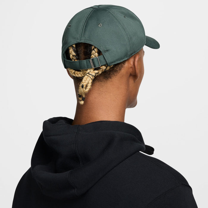 Nike Club Hat in dark green with adjustable strap and metal buckle, back view worn by person.