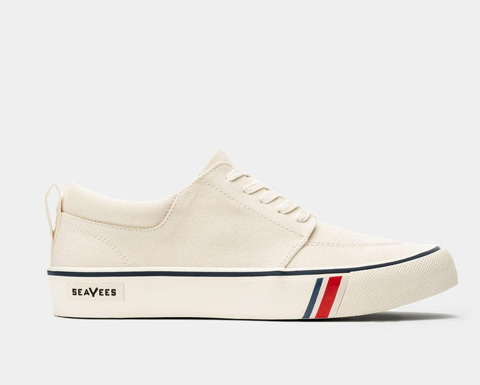 SeaVees Coastal Cruiser sneakers in cream canvas with blue and red stripe accents on the sole, side view.