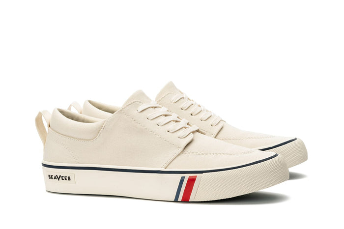 SeaVees Coastal Cruiser sneakers in cream canvas with lace-up closure, navy and red stripe detail on midsole, side perspective.
