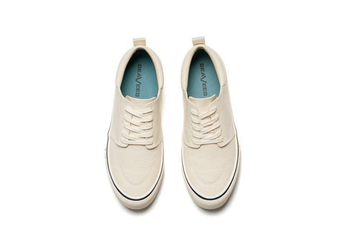 SeaVees Coastal Cruiser sneakers in off-white canvas with lace-up design and blue insoles, top view.