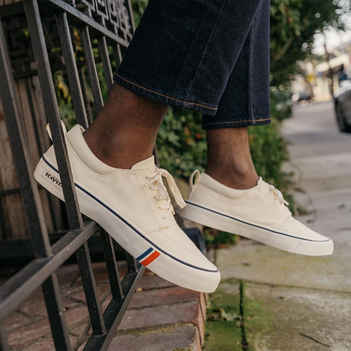 SeaVees Coastal Cruiser sneakers in off-white canvas with navy and red striped accents on midsole, streetwear lifestyle context