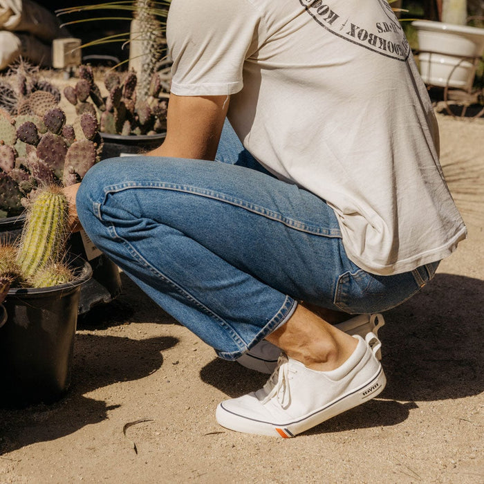 SeaVees Coastal Cruiser sneakers in white with canvas upper, rubber sole, and colorful stripe detail, worn outdoors near cacti.