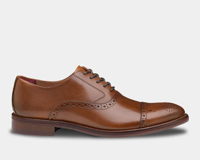 Johnston & Murphy Conard Cap Toe dress shoes in tan leather with brogue detailing and stacked heel, side view.
