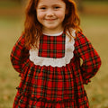 Young girl wearing a red plaid dress with a white collar in an outdoor setting