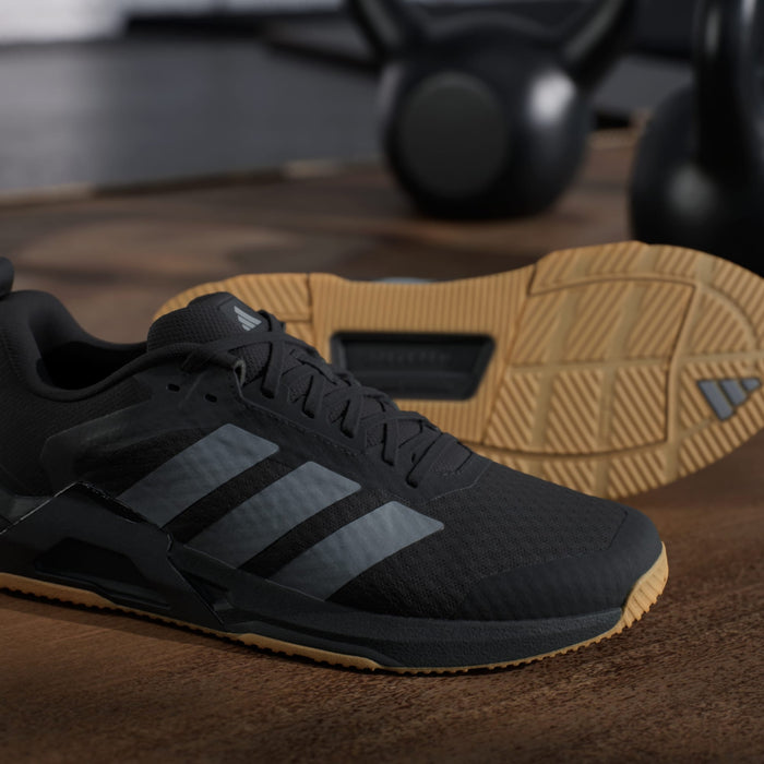 Adidas Dropset Control Trainer shoes in black with gray accents and gum rubber outsole, displayed on a wooden floor.
