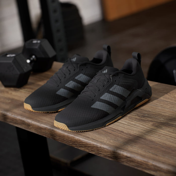 Adidas Dropset Control Trainer shoes in black with gray stripes and gum sole, side angle on wooden surface.