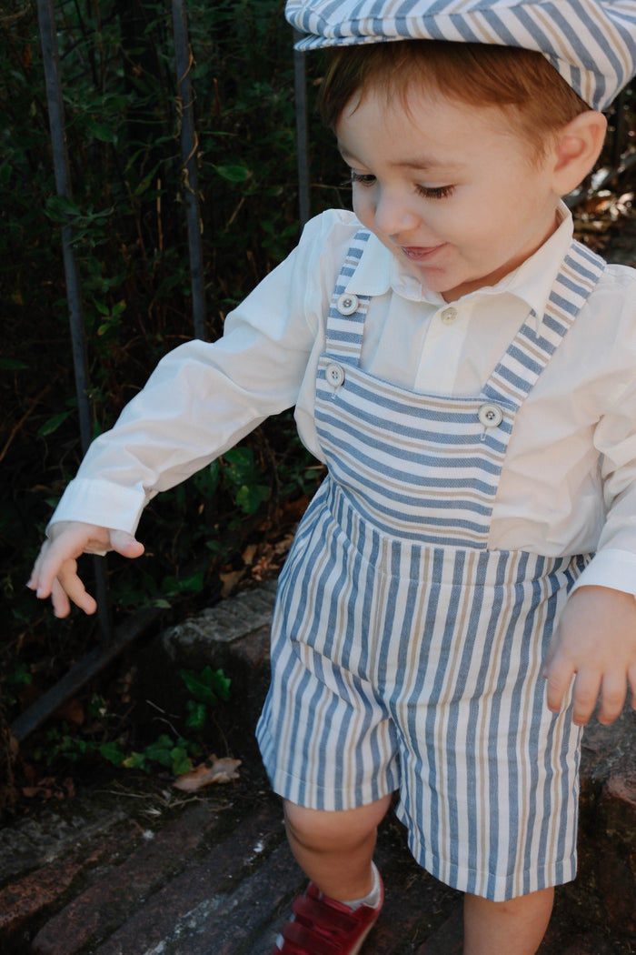 Child wearing a blue and white striped outfit with a matching hat outdoors.