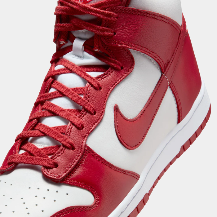 Nike Dunk High Retro SE sneakers close-up showing red leather overlays, white base, matching red laces, and Nike Swoosh detailing.