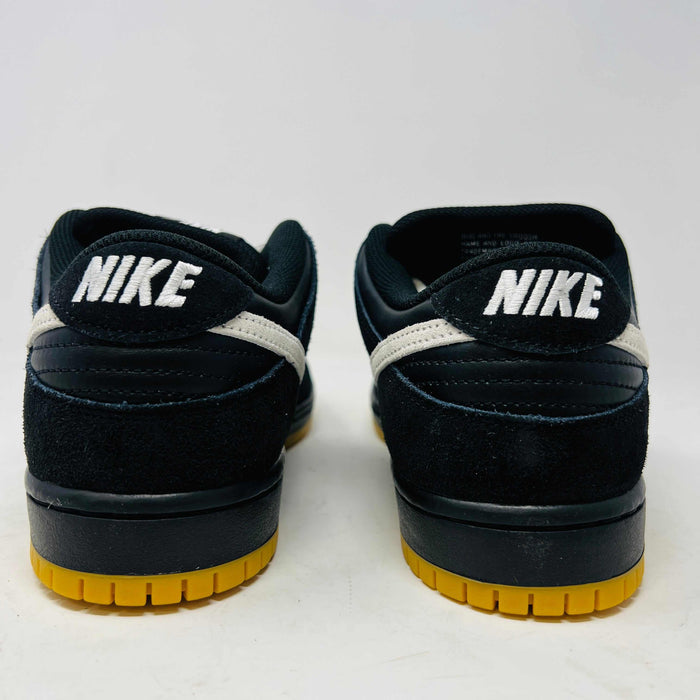 A black Nike Dunk Low Pro SB Black White Gum sneaker with white laces and swoosh sits on a purple Nike SB box. The 2025 shoe has a yellow sole, leather-texture finish, and both are in new condition.