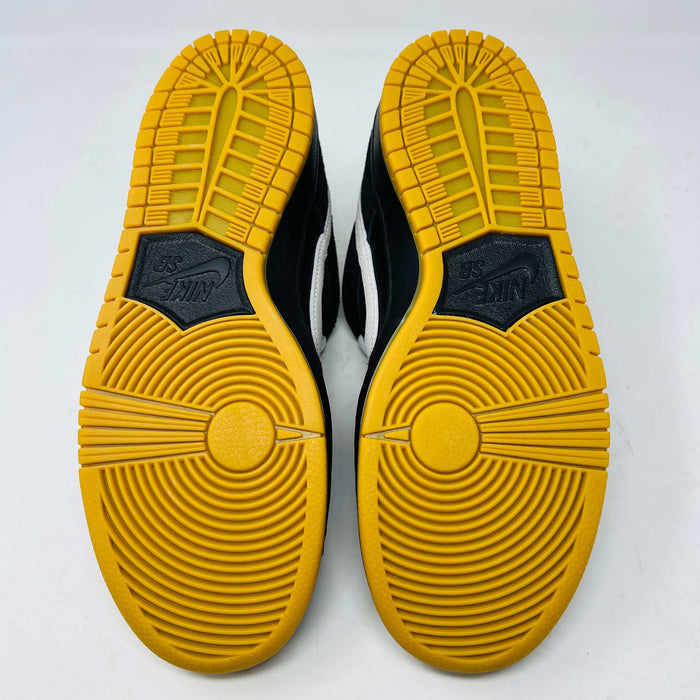 A black Nike Dunk Low Pro SB Black White Gum sneaker with white laces and swoosh sits on a purple Nike SB box. The 2025 shoe has a yellow sole, leather-texture finish, and both are in new condition.