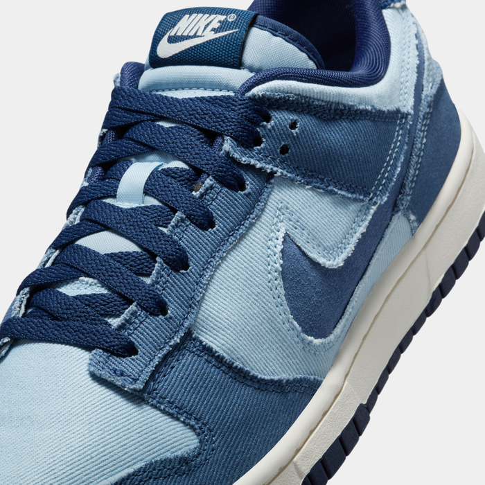 Nike Dunk Low Retro SE sneakers in light blue and navy with textured denim material, close-up of laces and side logo.