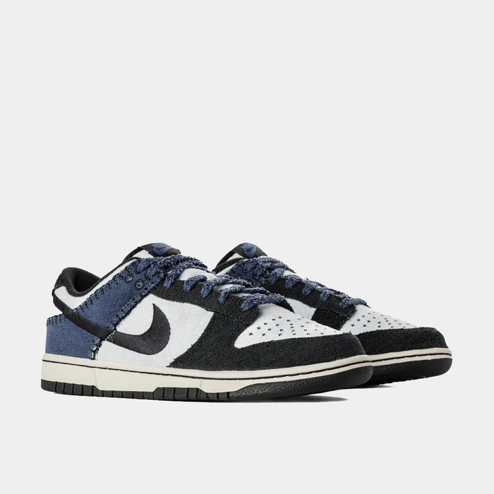 Nike Dunk Low Retro sneakers with textured black, white, and blue panels, frayed edges, and perforated toe box, angled front view.