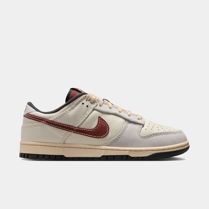Nike Dunk Low sneakers in cream and light gray leather with dark red Swoosh, beige laces, and black rubber outsole, side view.