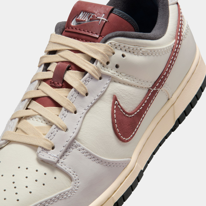 Nike Dunk Low sneakers in cream and maroon featuring leather upper, contrast stitching, and lace-up closure, angled view.