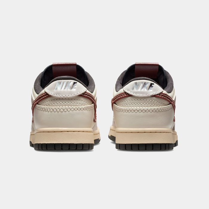 Nike Dunk Low sneakers back view showing beige leather upper with maroon accents, black outsole, and Nike branding on heel.