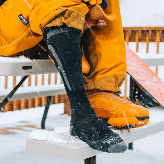 Darn Tough Edge Over-the-Calf Midweight Ski & Snowboard Socks in black with gray accents, worn in snowy outdoor setting.