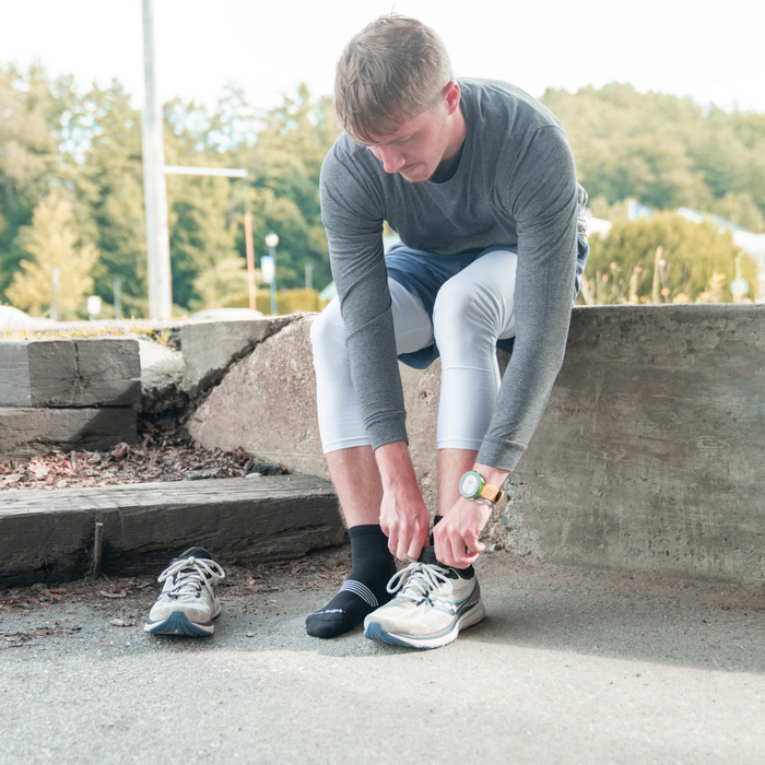 Darn Tough Element Quarter Lightweight Running Sock in black with white stripe accents, worn by a person tying running shoes outdoors.
