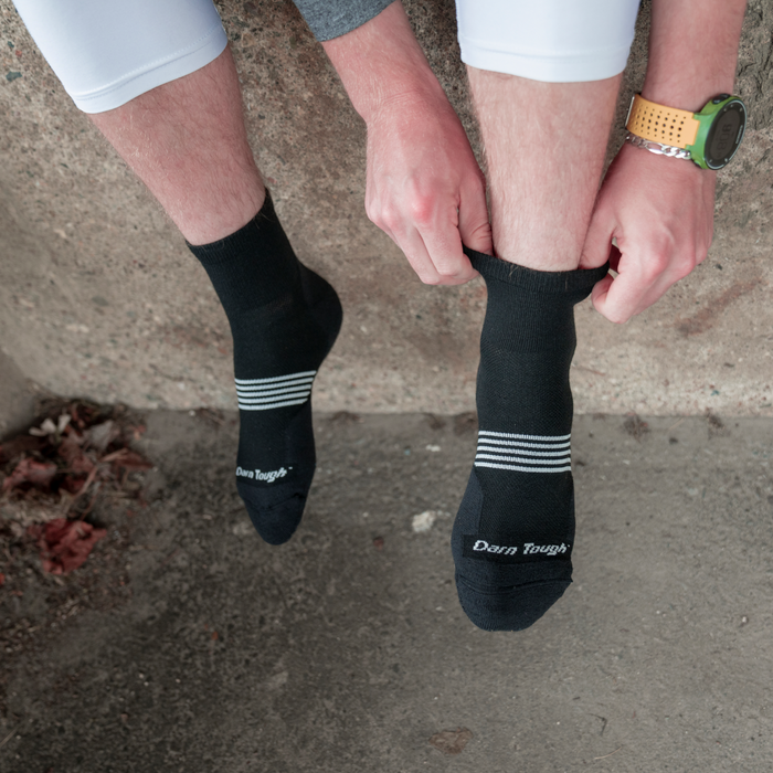 Darn Tough Element Quarter Lightweight Running Sock in black with white stripe accents and reinforced toe, worn outdoors.
