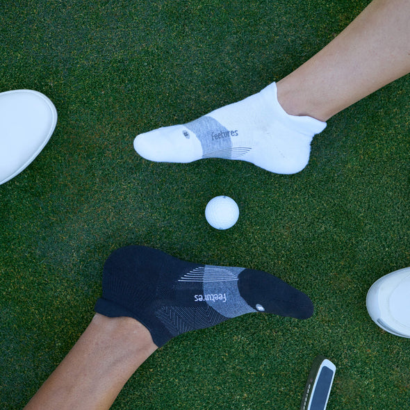 Feetures Elite Golf Max Cushion No Show Tab socks in black and white, worn by golfers on green.