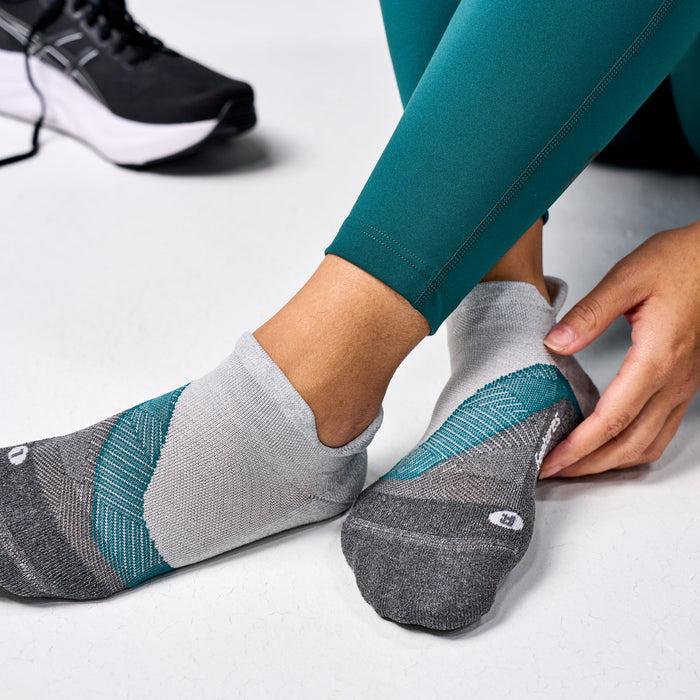 Feetures Elite Light Cushion No Show Tab socks in gray and teal, worn by person adjusting fit.
