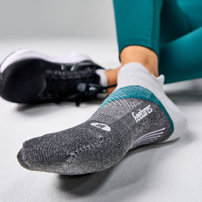 Feetures Elite Light Cushion No Show Tab socks in gray with teal accents, worn by person sitting.