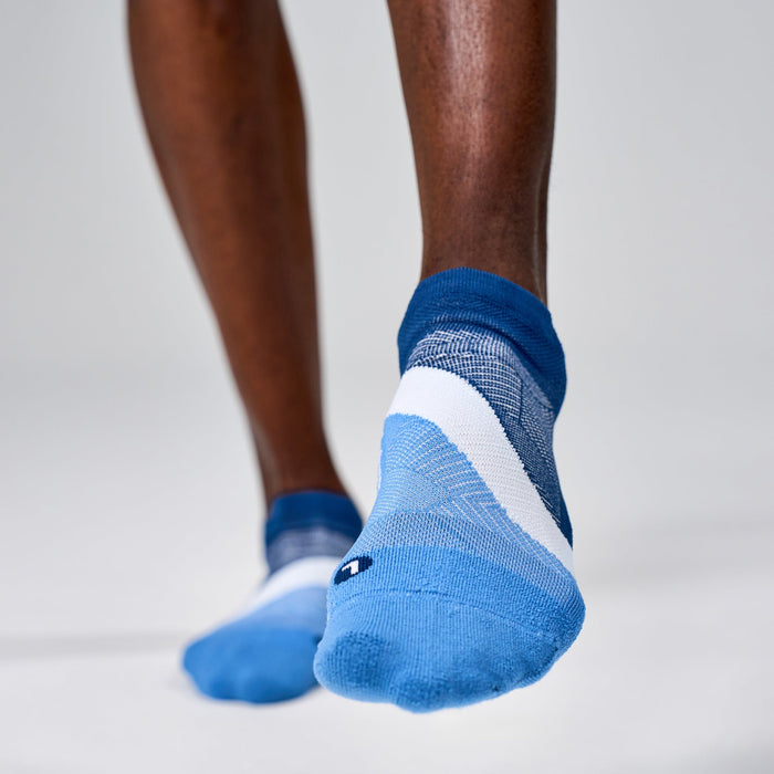 Feetures Elite Light Cushion No Show Tab socks in blue and white with arch band, worn by person standing.