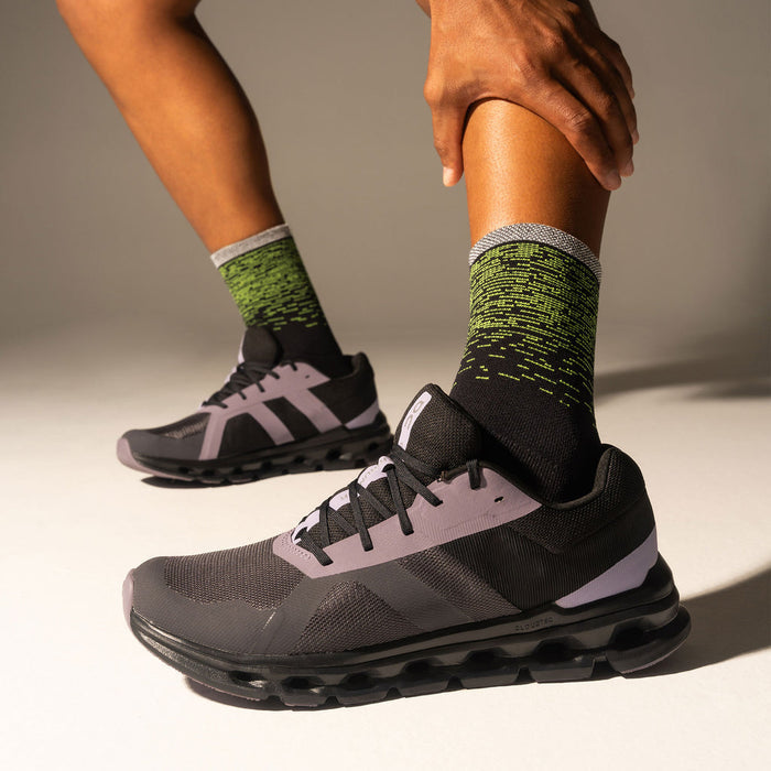 Feetures Elite Light Cushion Reflective Mini Crew socks in black with neon green reflective design and gray cuff, worn by runner.
